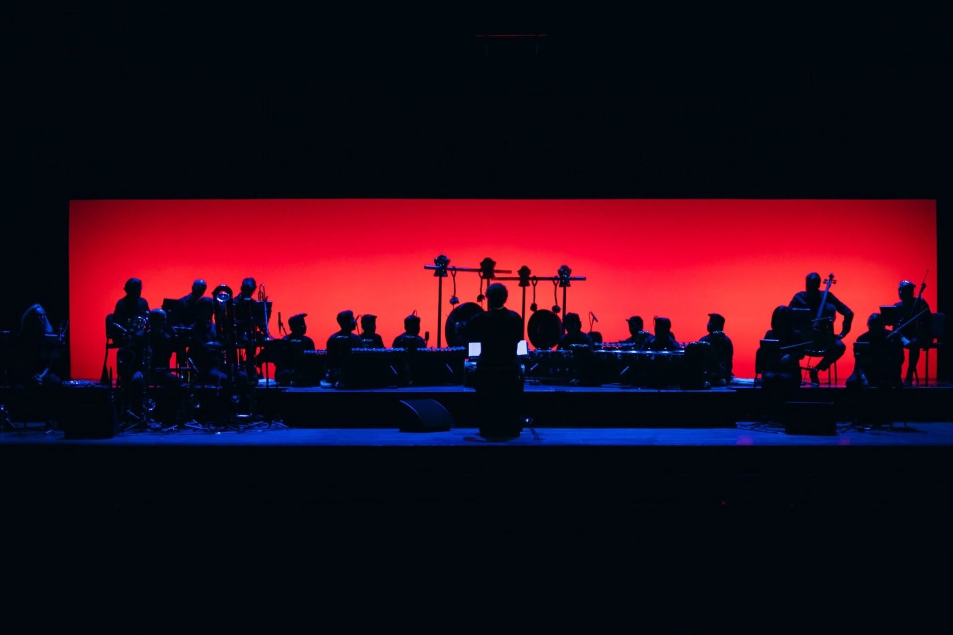 Ed Liebrecht conducting Het Muziek and Gamelan Salukat in silhouette against a red stage